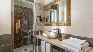 Un baño moderno con ducha de vidrio, un espejo grande, un lavamanos tipo recipiente y toallas dobladas con cuidado.