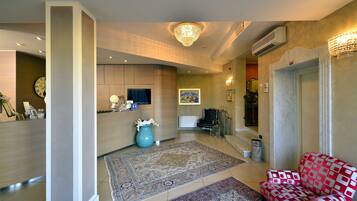 A spacious lobby with a reception desk, a large chandelier, a patterned rug, and a red patterned armchair.