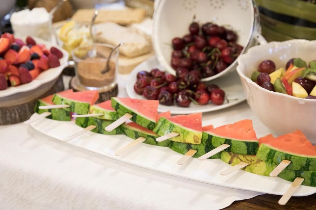 Una mesa de buffet con brochetas de sandía, cuencos de fruta y diversos postres.