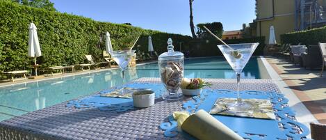 A poolside table with a bottle of champagne, a martini glass, and a bowl of snacks.