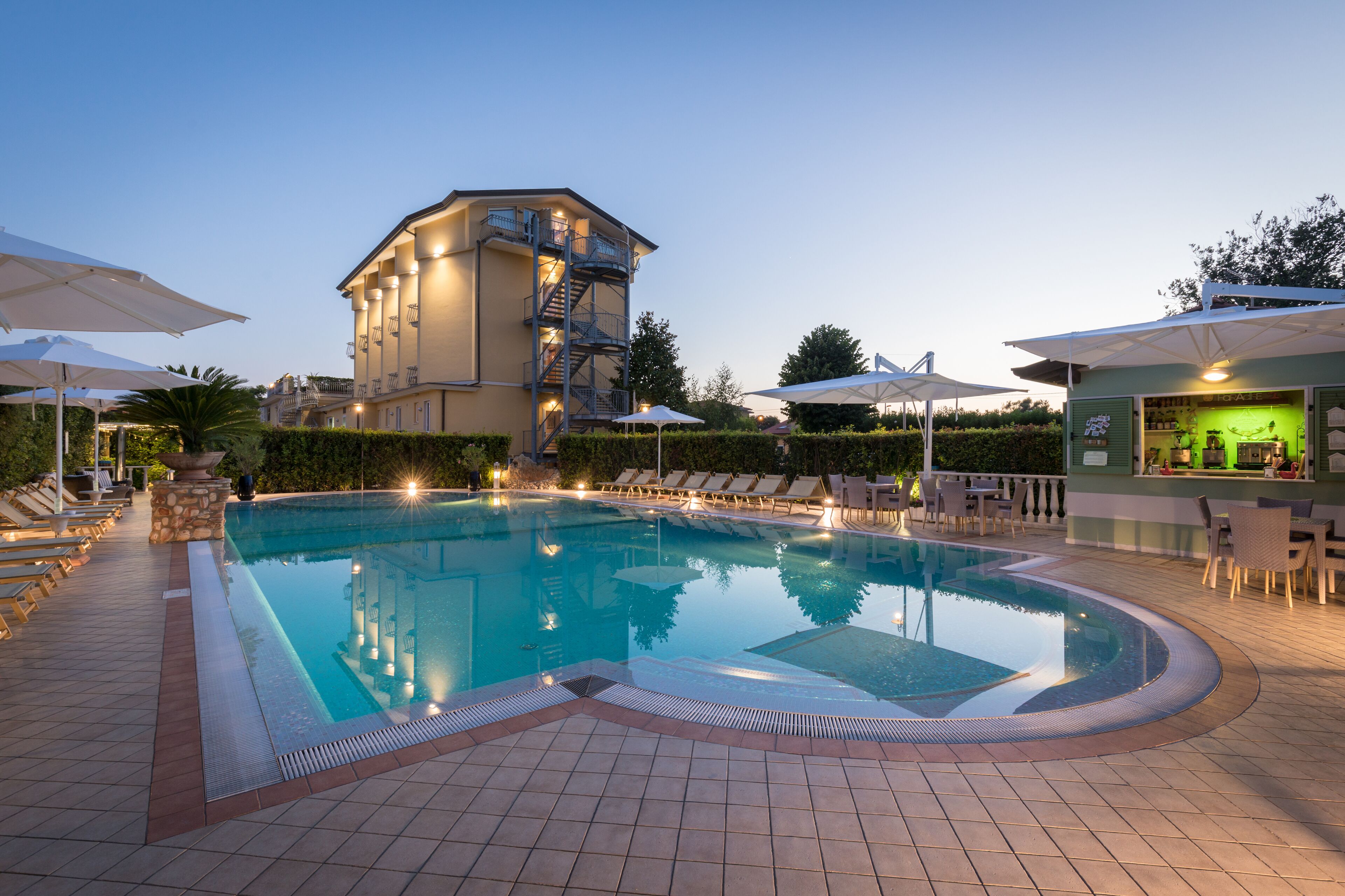 A swimming pool with lounge chairs and umbrellas, a bar area, and a building with a staircase.