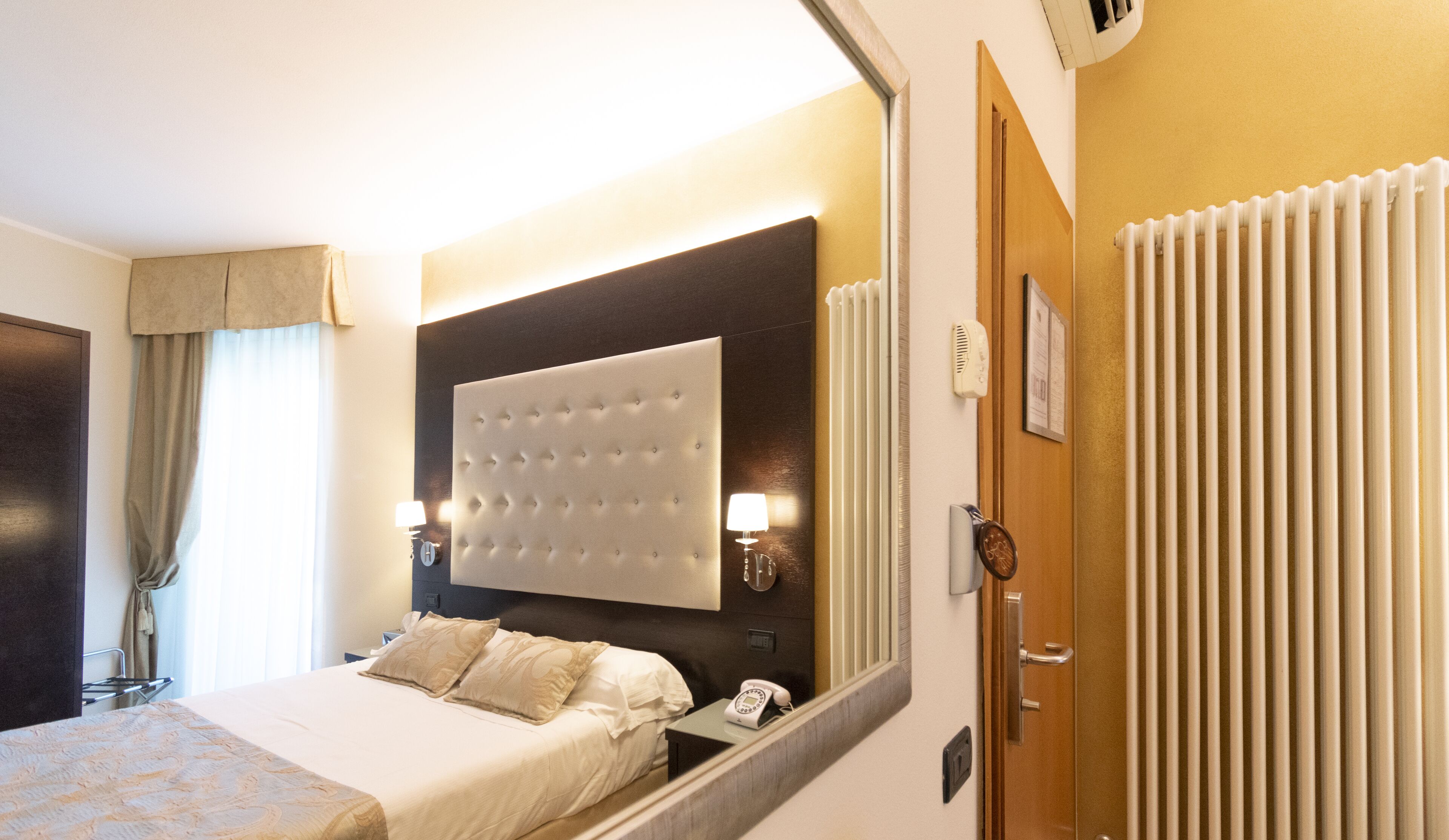 A hotel room with a large bed, a headboard with a tufted design, bedside lamps, a telephone, and a radiator.