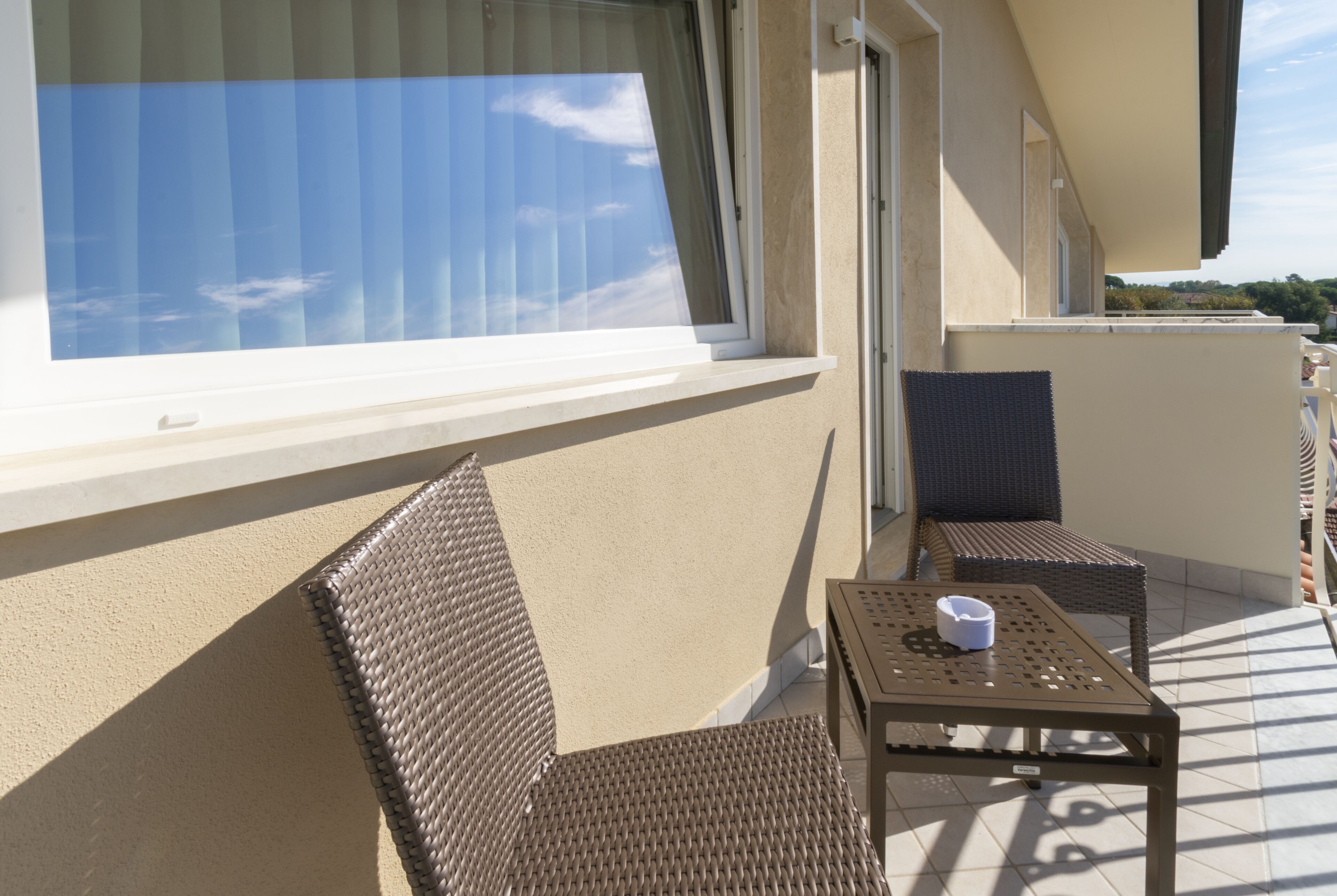 A balcony with wicker furniture, a table, and a window overlooking a clear sky.