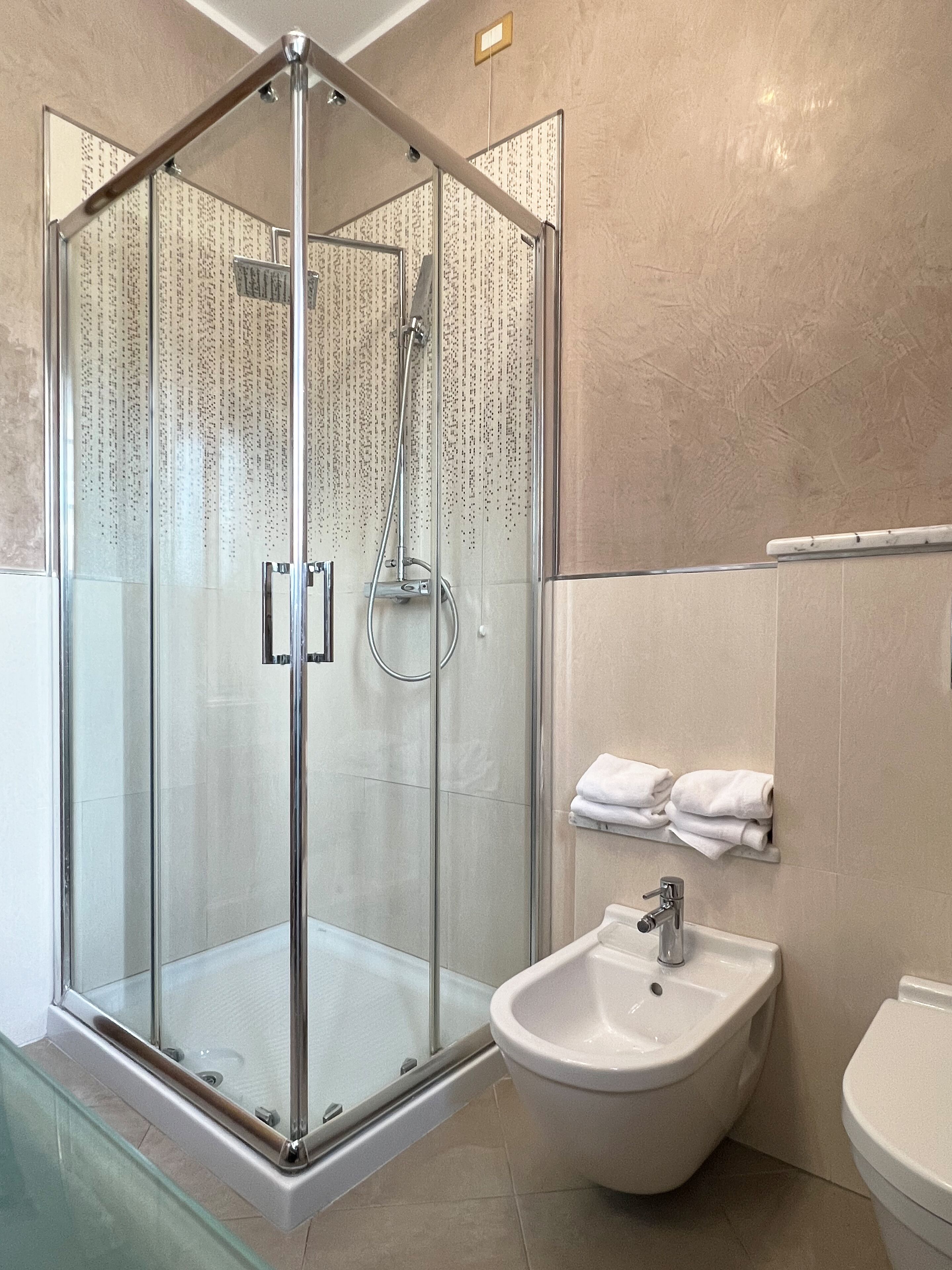 Een moderne badkamer met een douche met glazen wand, een bidet en een toilet.