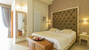 Une chambre d’hôtel avec un grand lit, une table de chevet en bois, une petite table de chevet sur laquelle se trouve un plateau de petit-déjeuner, un miroir avec un cadre décoratif et un radiateur.