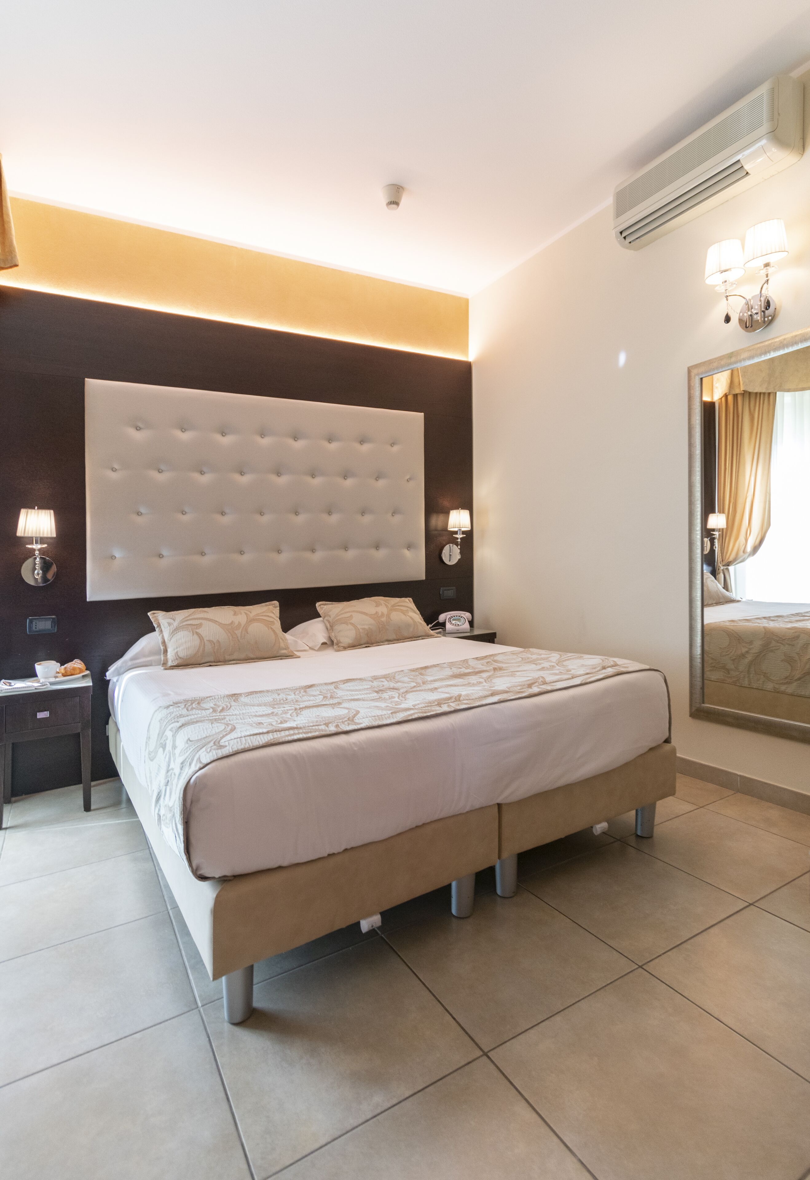 Une chambre d’hôtel moderne avec un grand lit, un climatiseur fixé au mur et un grand miroir.