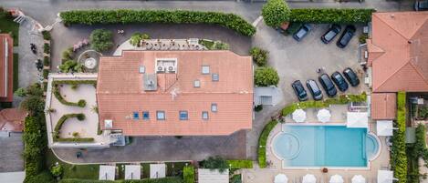 Vue aérienne d’un quartier résidentiel avec une grande maison dotée d’un toit en tuiles, d’une piscine et d’un court de tennis.
