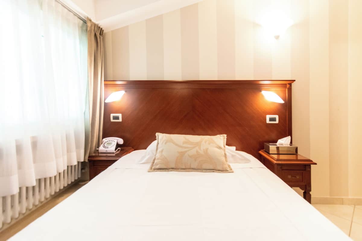 A hotel room with a large bed, wooden headboard, two bedside tables, a telephone, and a nightstand with a tissue box.