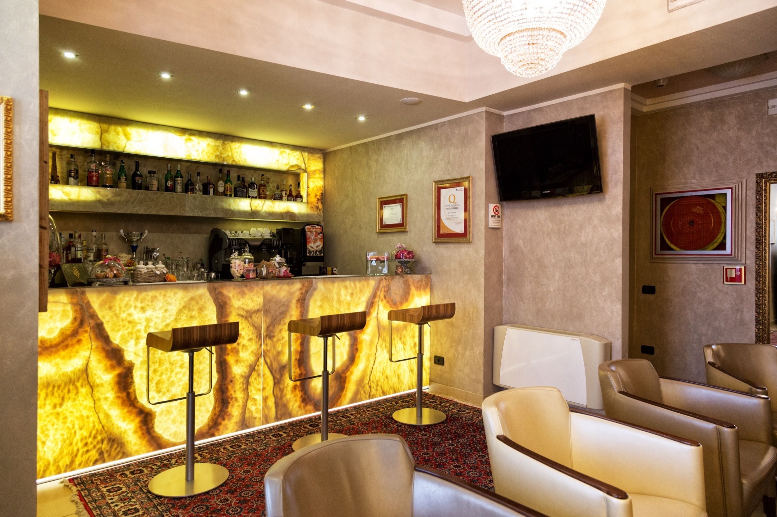 A bar area with a marble countertop, bar stools, and a television mounted on the wall.