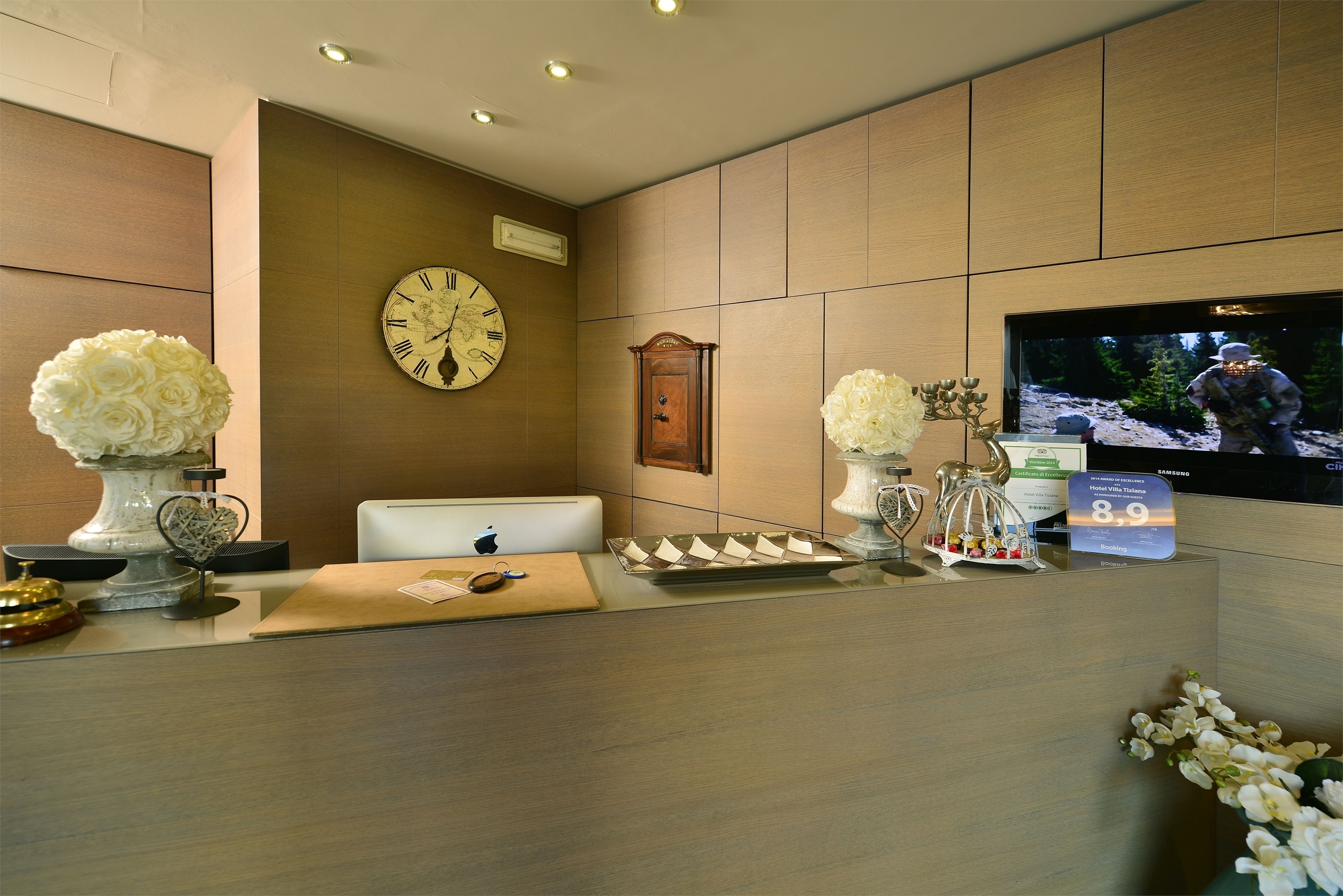 A hotel reception desk with a clock, a television, and decorative vases.
