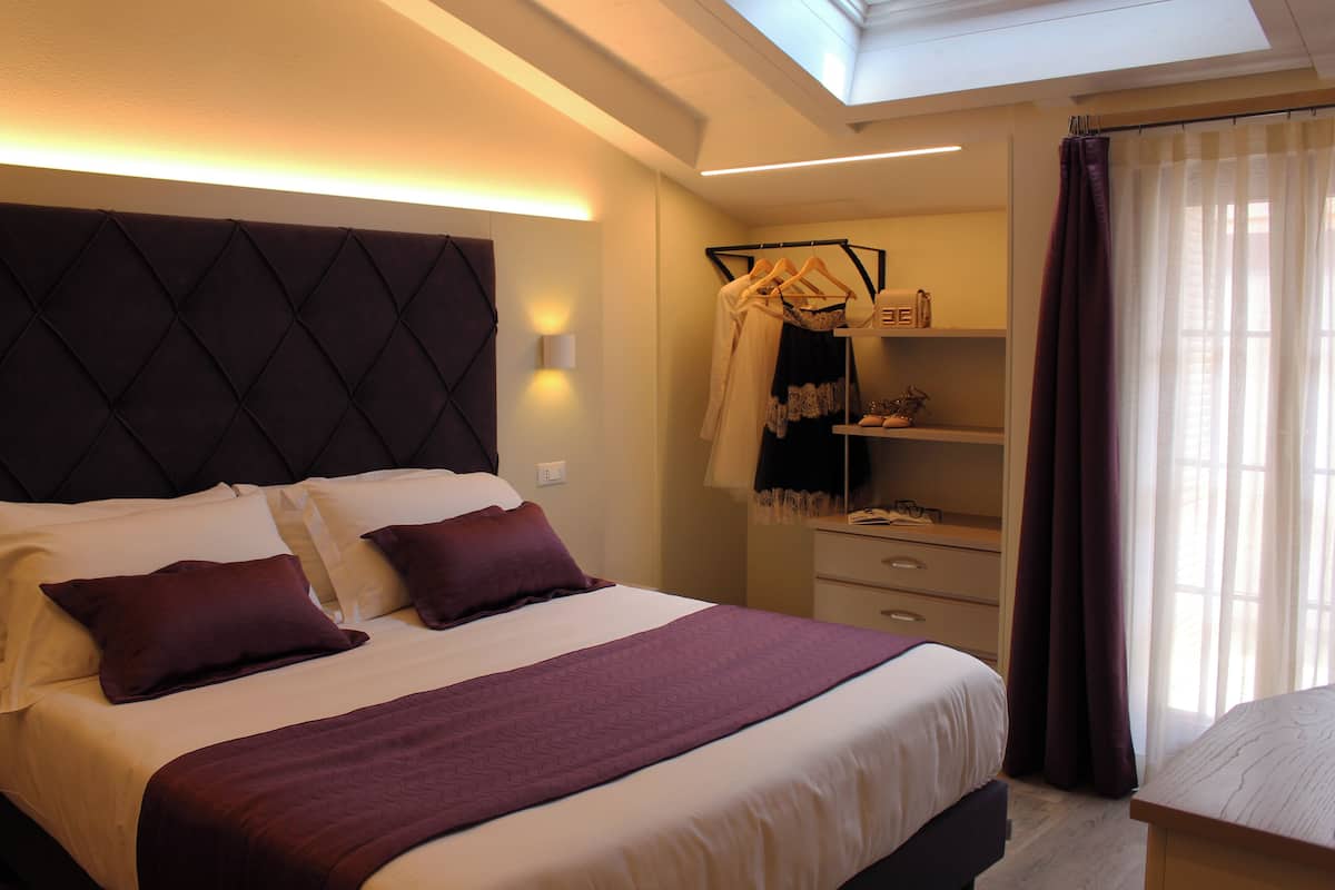 A hotel room with a large bed, a wardrobe, a mirror, and a window with curtains.