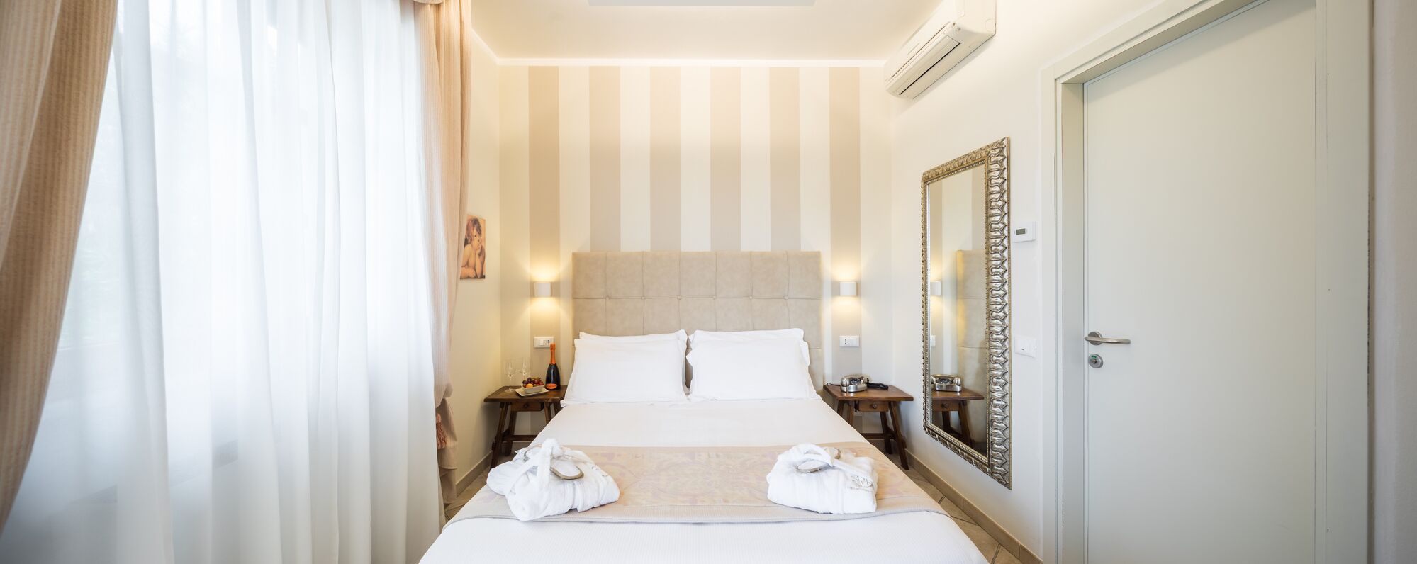 A hotel room with a large bed, two bedside tables, a mirror, and a door.