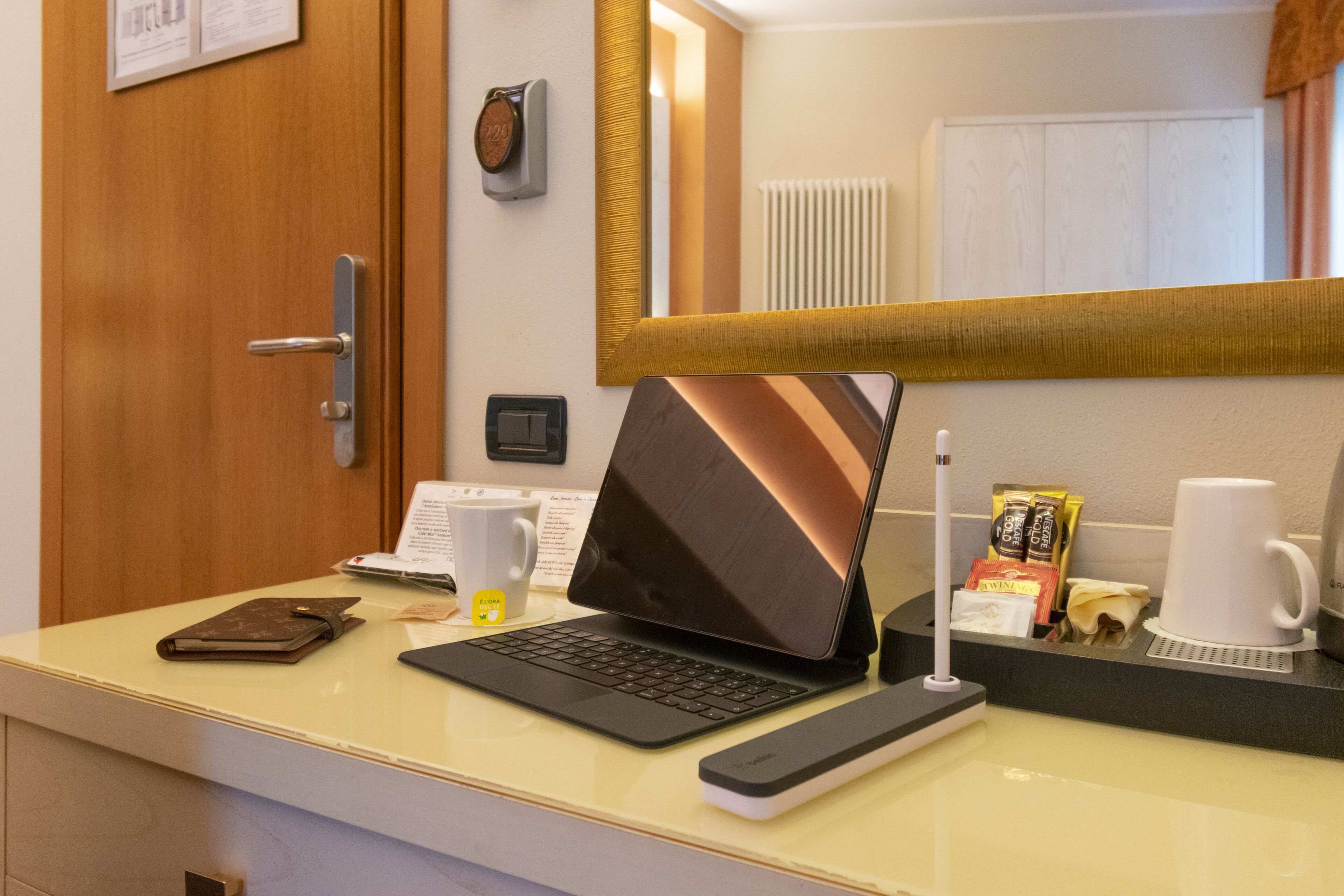Balcão de recepção de hotel com um laptop, uma xícara de café, um controle remoto e uma pequena planta.