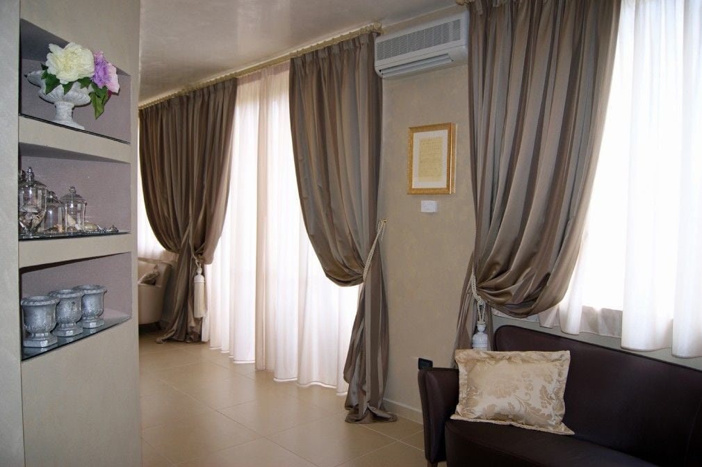 A living room with a sofa, a decorative shelf with vases, and a large window with curtains.