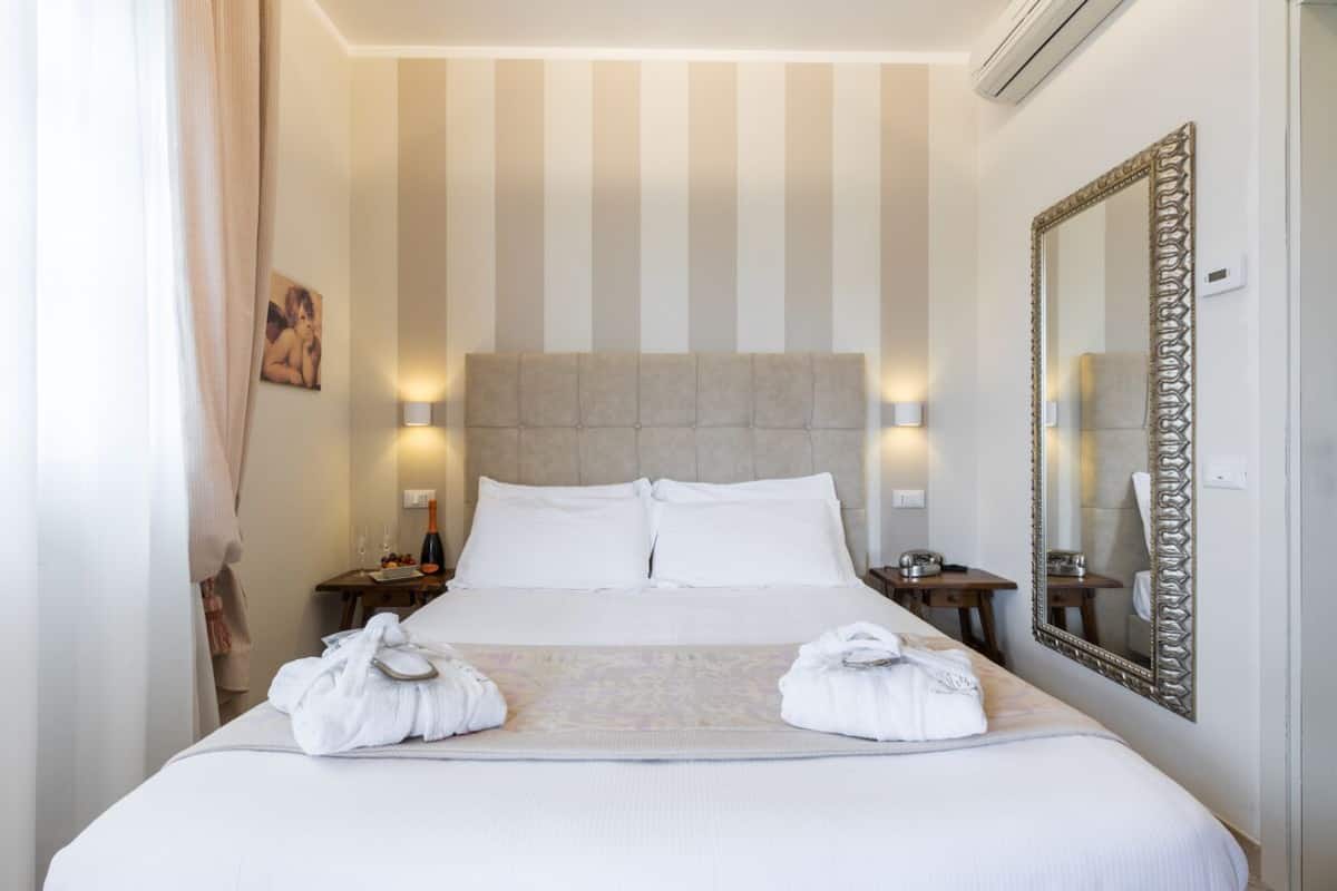 A hotel room with a large bed, two bedside tables, a mirror, and a striped wall.