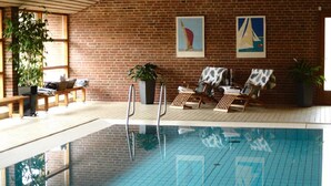 Una piscina interior con pared de ladrillo, sillones de descanso y obras de arte.