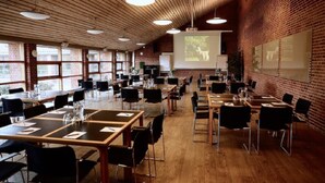 Un salón de conferencias con mesas y sillas de madera, una pantalla de proyector y paredes de ladrillo.