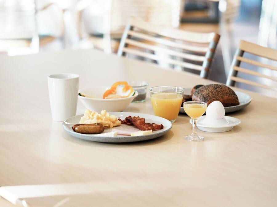 A breakfast setting with plates of eggs, bacon, and toast, a glass of orange juice, and a white mug on a wooden table.
