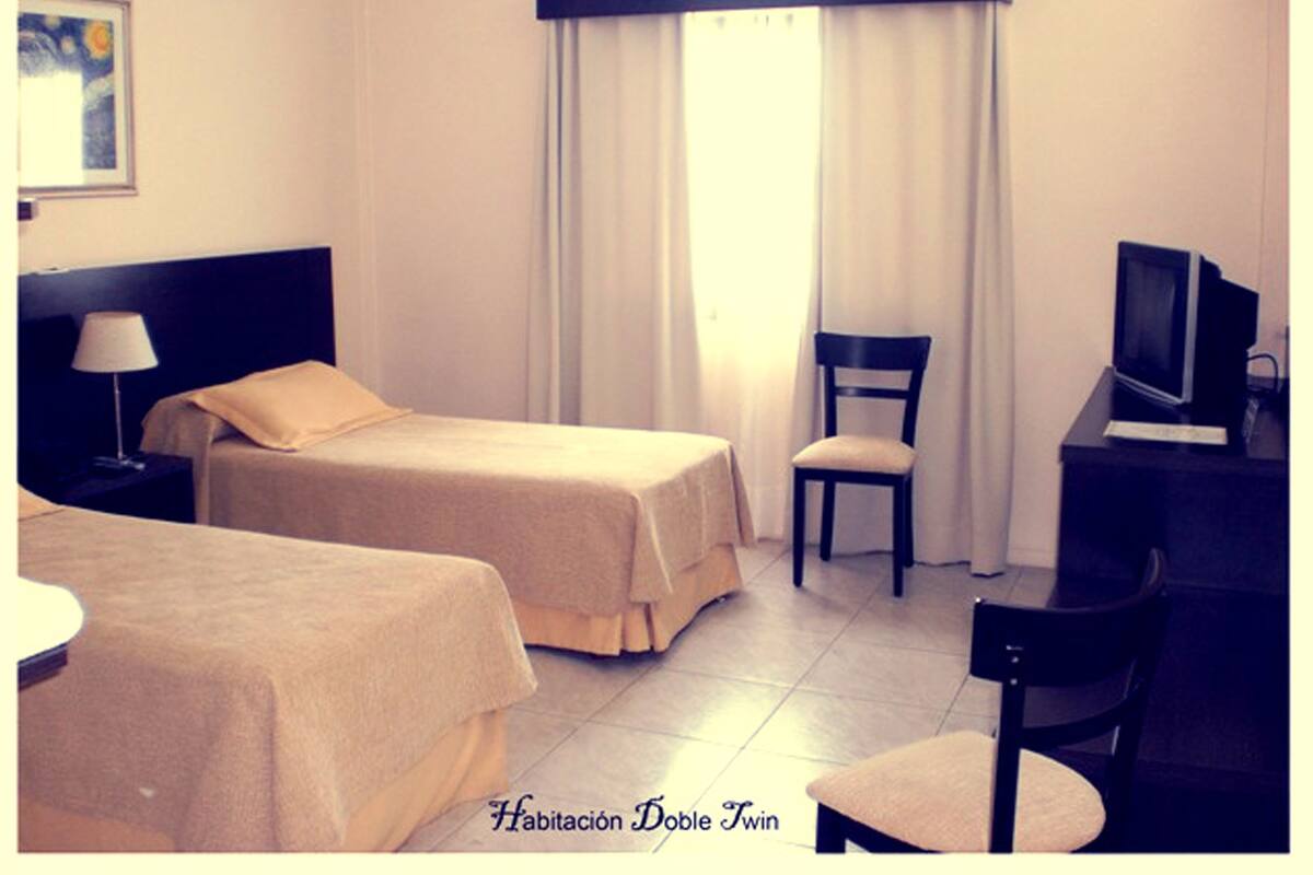 A hotel room with two beds, a desk with a computer, a chair, and a window with curtains.