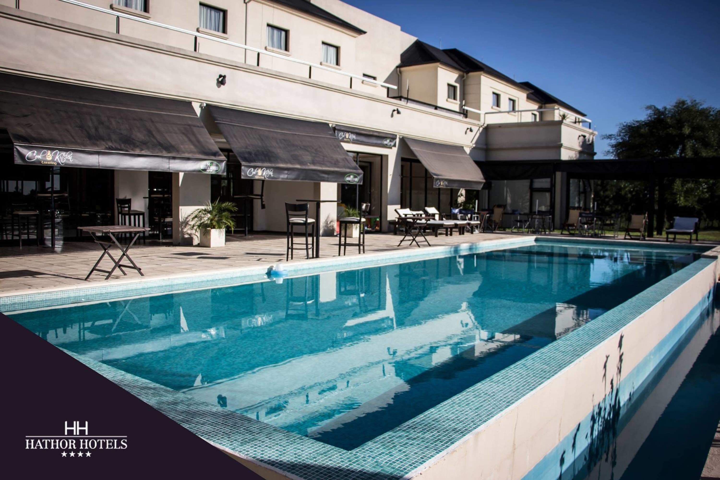 A hotel with a swimming pool, outdoor seating, and a covered patio area.