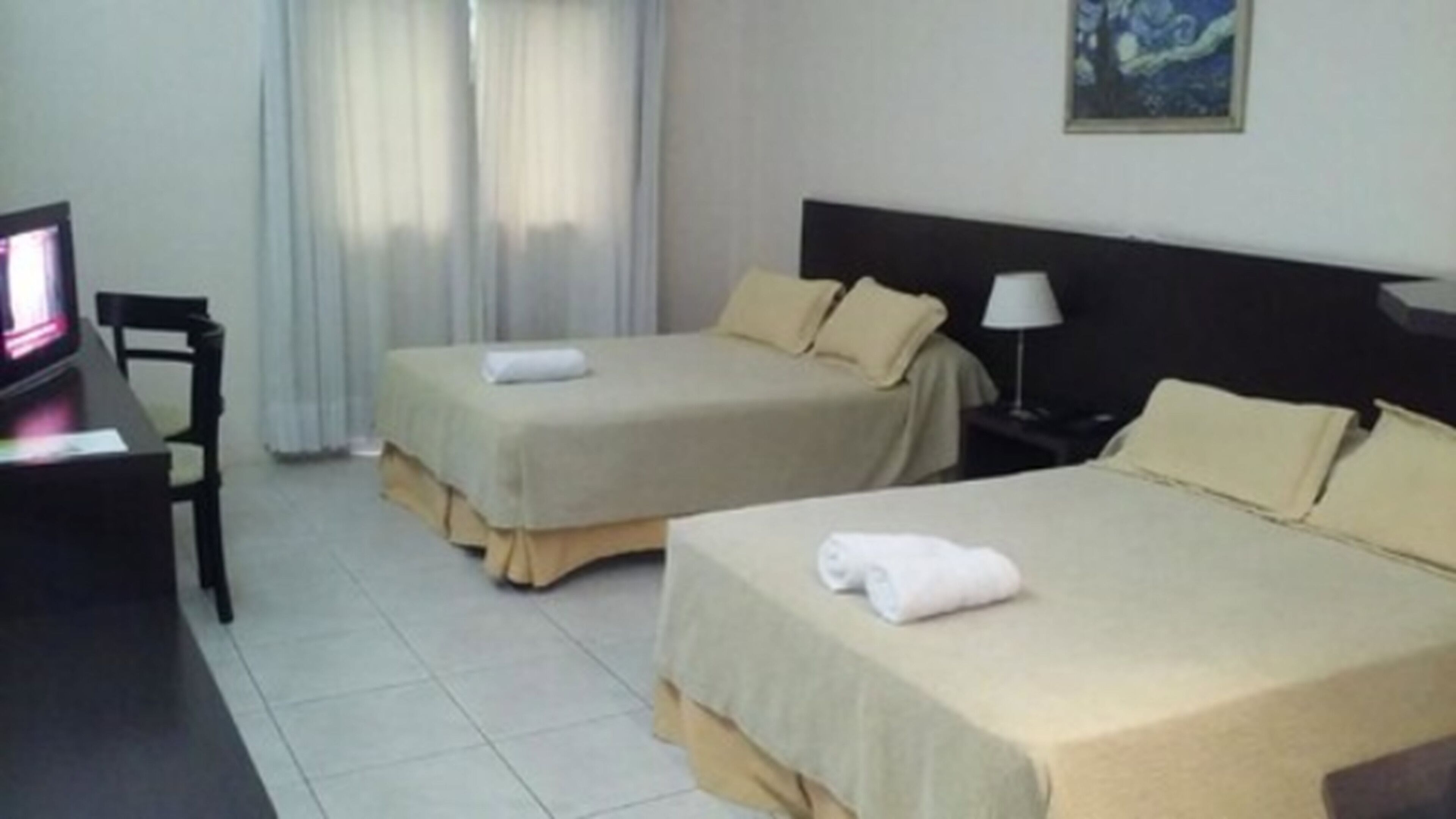 Habitación de hotel con dos camas, un escritorio con computadora y una mesita de noche con lámpara.