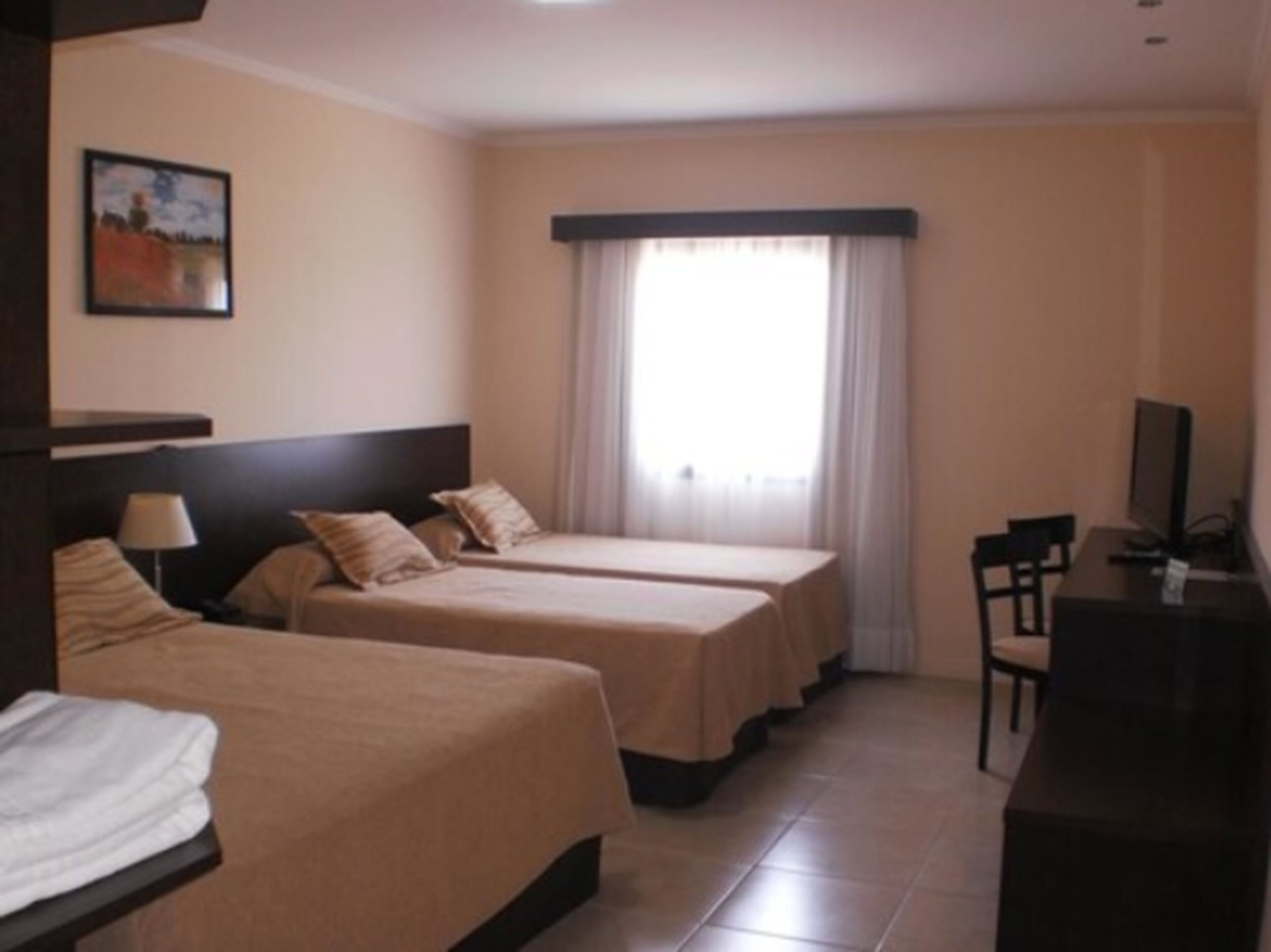 A hotel room with two beds, a desk, a chair, a television, and a window with curtains.