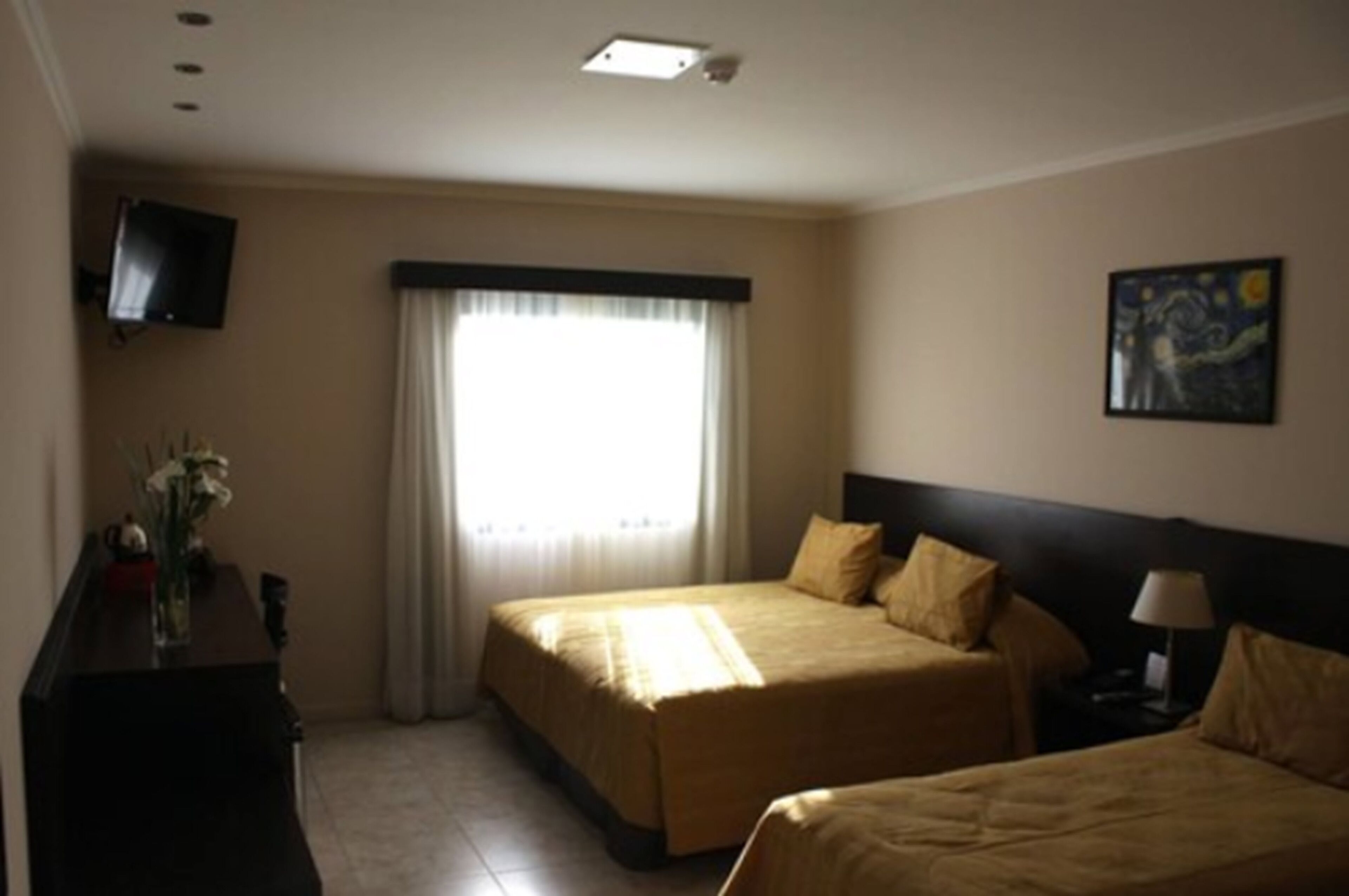 A hotel room with two beds, a flat-screen TV, a painting, and a window with curtains.