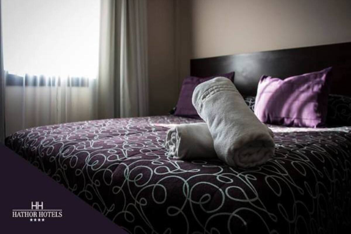 A hotel room with a bed, a headboard, and a window with curtains.