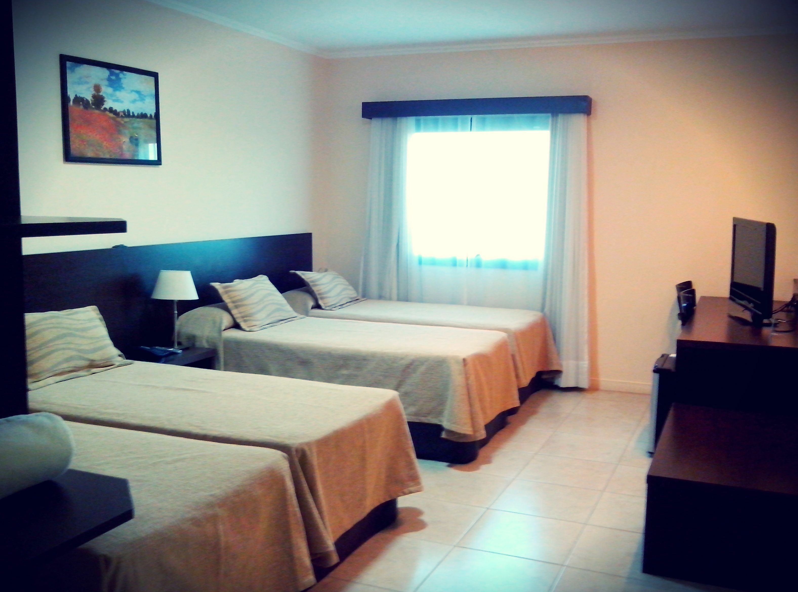 A hotel room with two single beds, a desk with a computer, and a window with curtains.