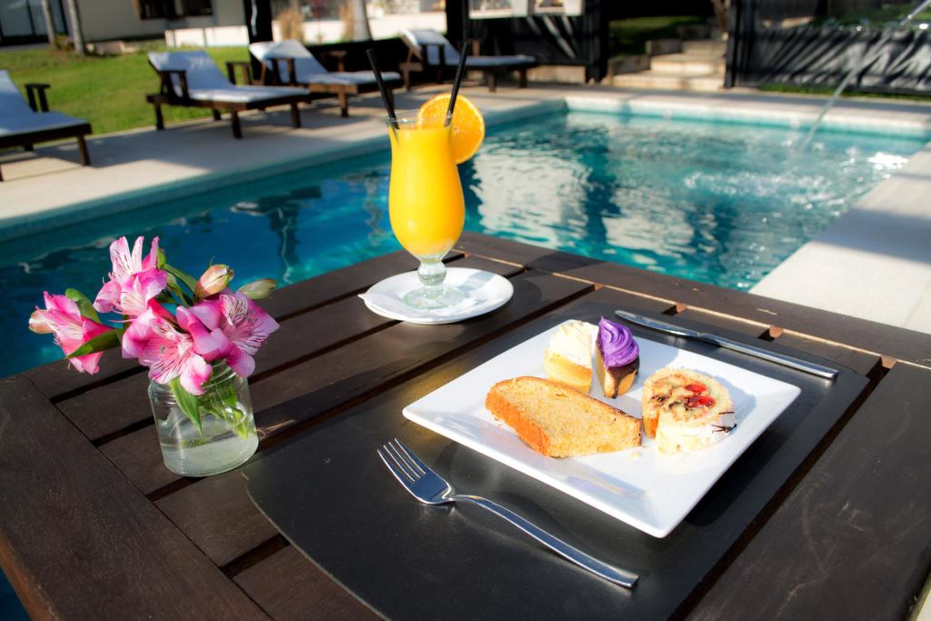 Un tavolo da pranzo con un piatto di cibo, una bevanda e un vaso di fiori vicino a una piscina.