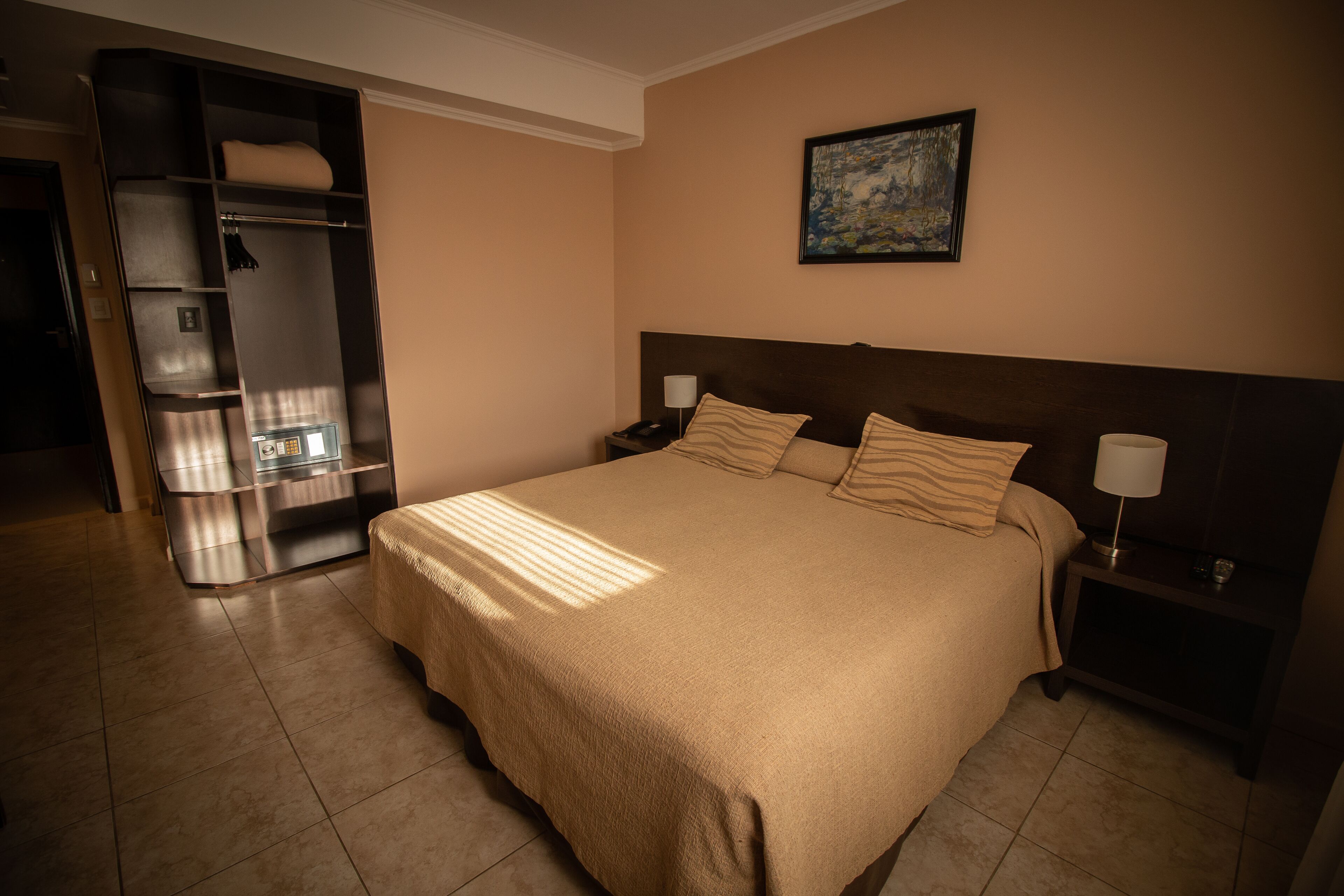 Een hotelkamer met een groot bed, een kledingkast, een nachtkastje en een schilderij aan de muur.