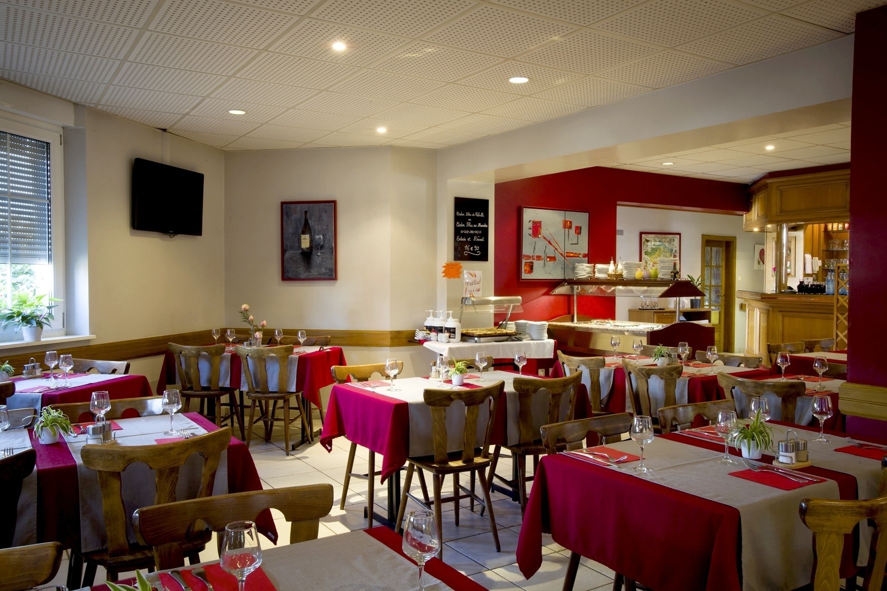 A restaurant with multiple tables, red tablecloths, and wooden chairs.