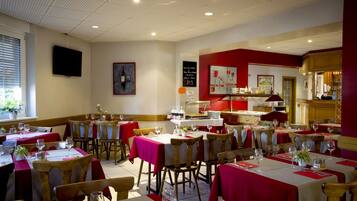 A restaurant with multiple tables, red tablecloths, and wooden chairs.