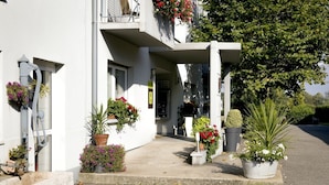 A white building with a covered entrance, potted plants, and hanging flower baskets. - Au Lion d'Or (Burnhaupt-le-Haut)