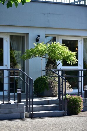 Un bâtiment avec un escalier menant à une porte, un petit arbre et un parterre de fleurs.