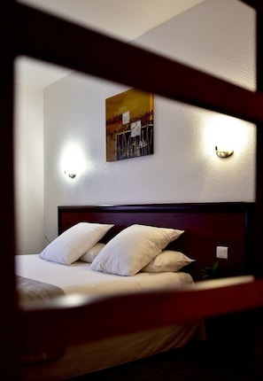 Habitación de hotel con una cama, almohadas blancas, cabecera y un cuadro en la pared.
