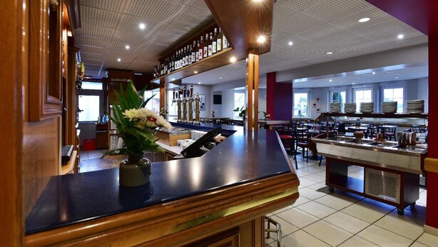 Een ruim restaurant met een bar, meerdere eettafels en een keuken op de achtergrond.