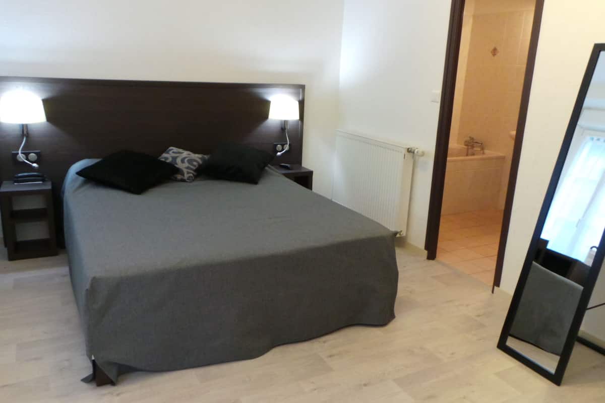 A bedroom with a large bed, two bedside tables with lamps, a mirror, and a radiator.
