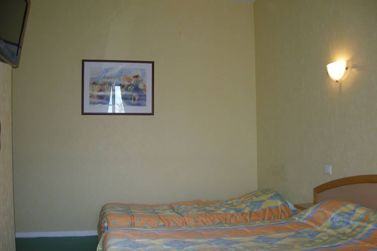 A room with a bed, a framed picture on the wall, and a wall-mounted light fixture.