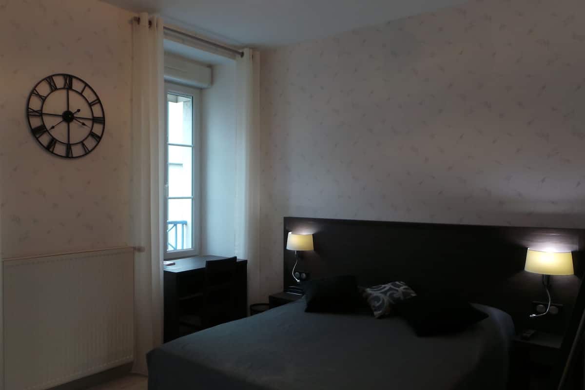 A bedroom with a bed, bedside lamps, a clock, and a window.