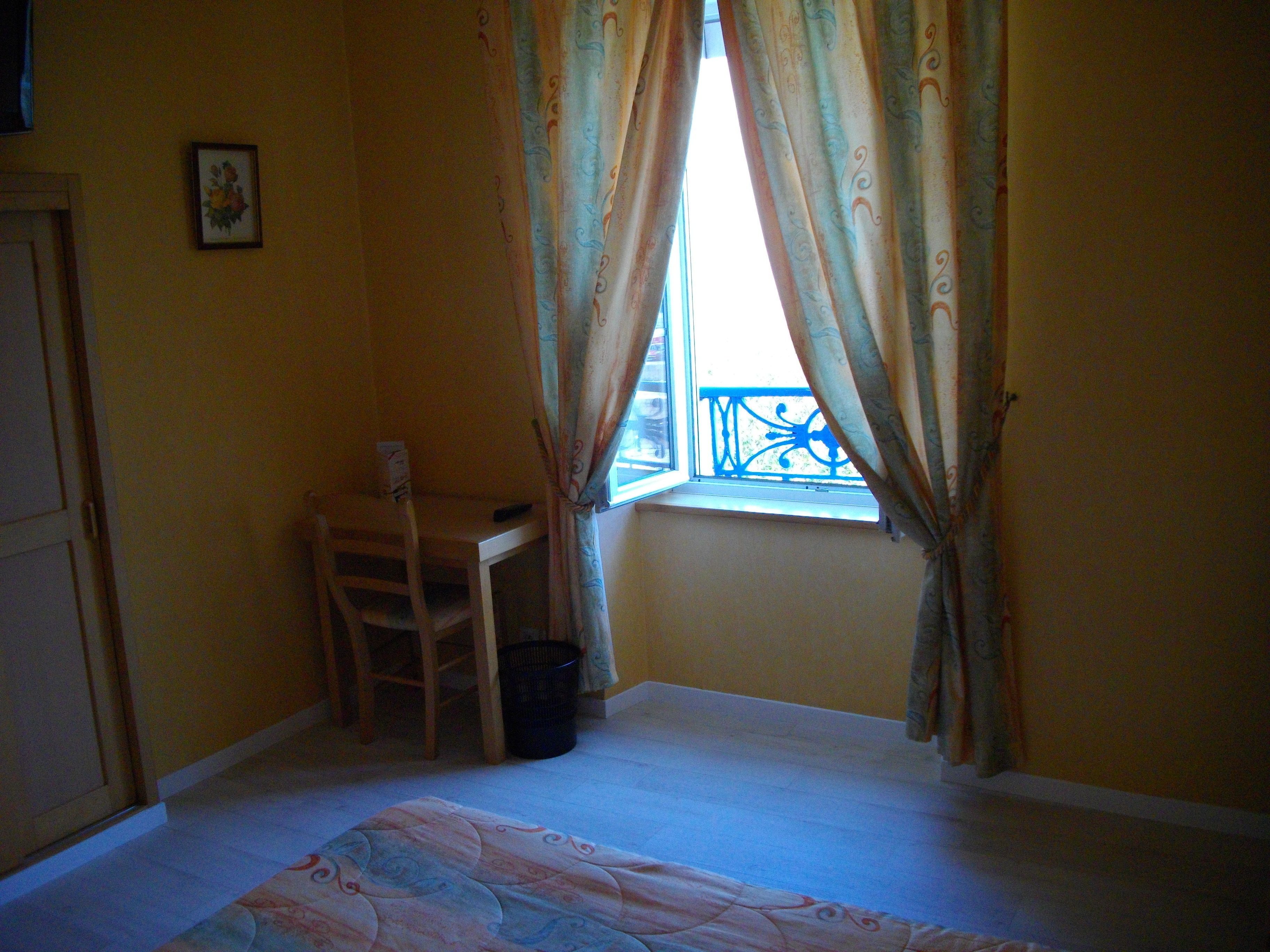 A room with a bed, a desk, and a chair near a window with curtains.