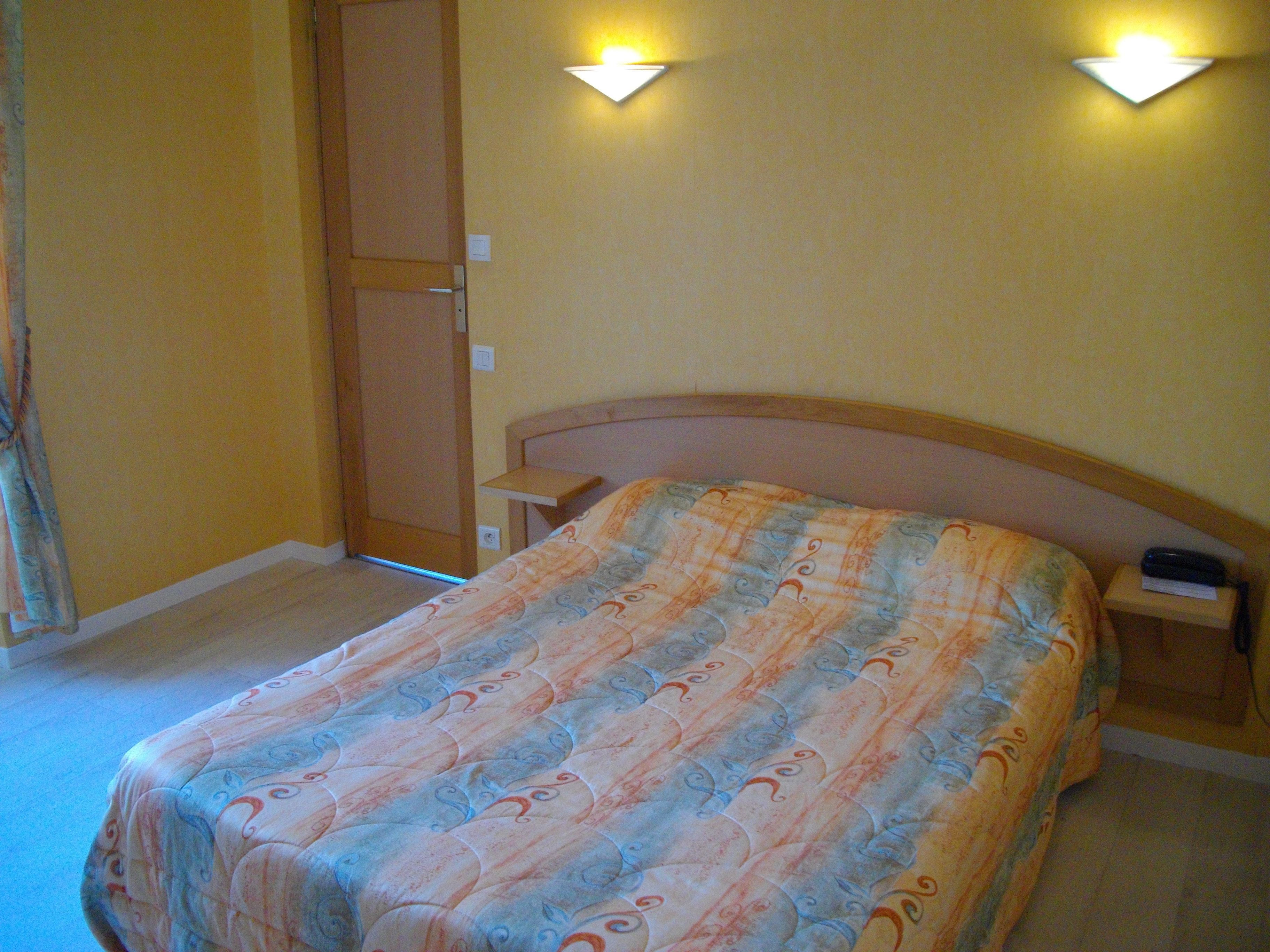 A bedroom with a bed, a nightstand, a lamp, and a wardrobe.