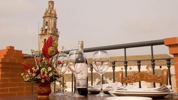 Una mesa de comedor con copas de vino, una botella y un arreglo floral, con vistas a una torre histórica.