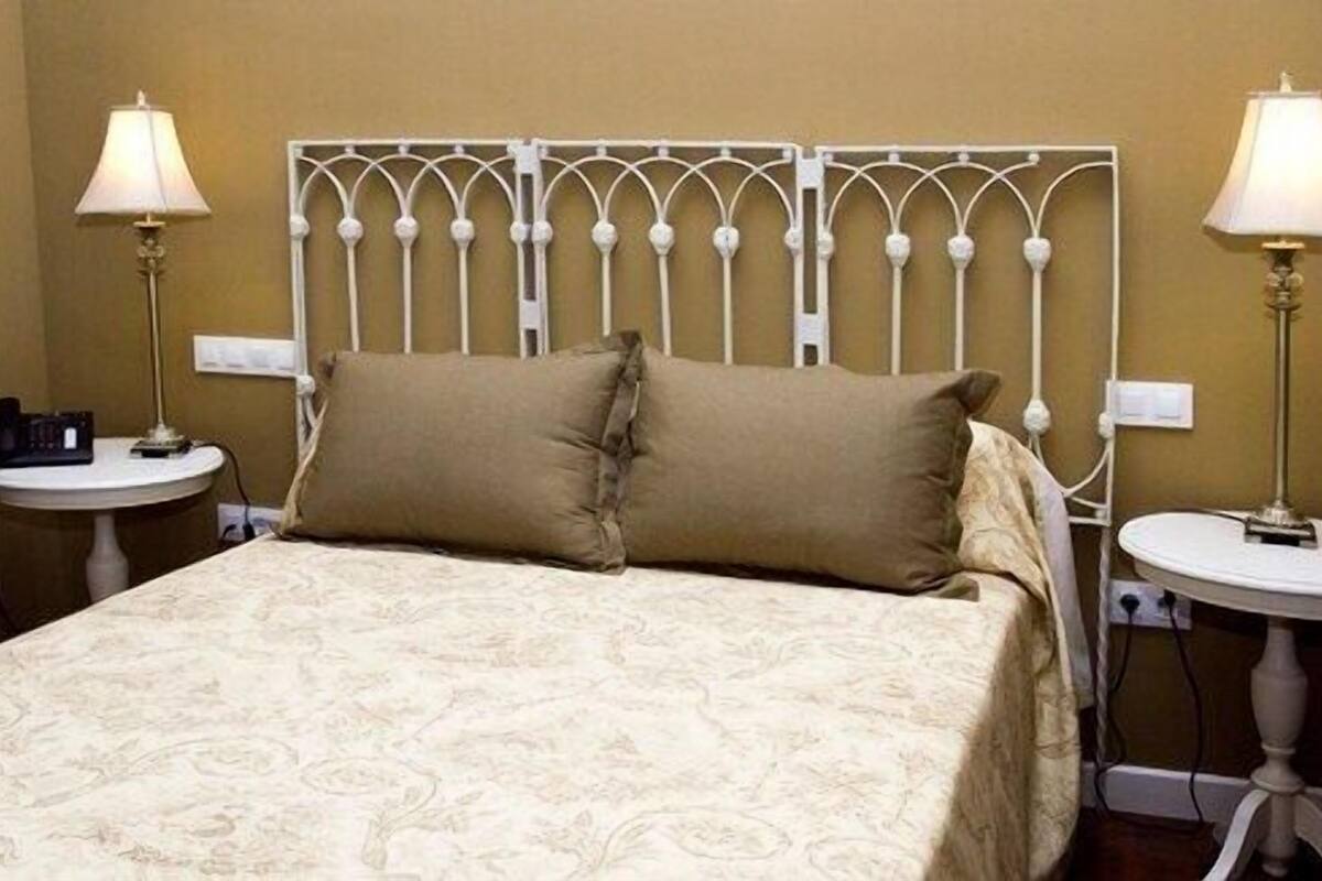 A neatly made bed with a patterned bedspread, two bedside lamps, and a decorative metal headboard.