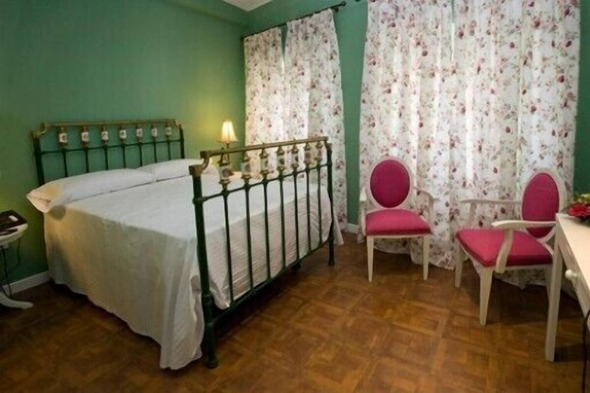 A room with a bed, two chairs, a table, and a lamp.