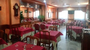 A restaurant with multiple tables covered in red tablecloths, wooden chairs, and a bar area with a mirror and clock. - Hostal Sancho Garcia (Espinosa de los Monteros)