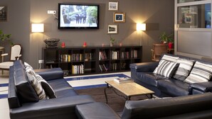 A modern living room with a large flat-screen TV, a bookshelf, a sofa, and a coffee table. - Le Carmin (Vitry-sur-Seine)