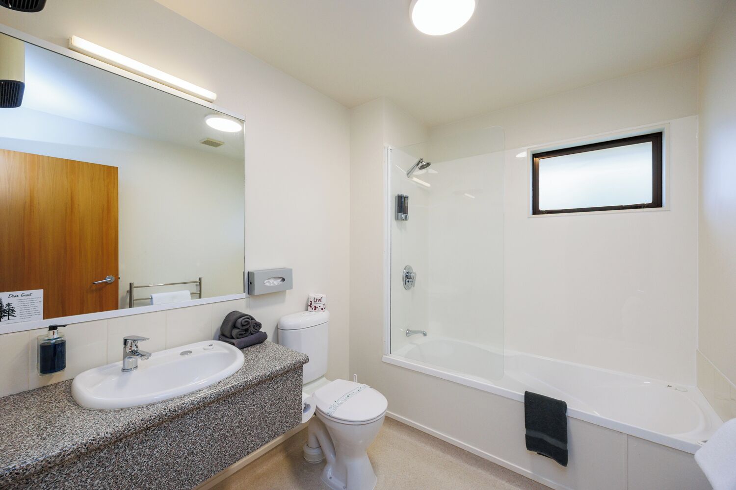 A modern bathroom with a granite countertop, a white sink, a toilet, a glass-enclosed shower, and a large mirror.