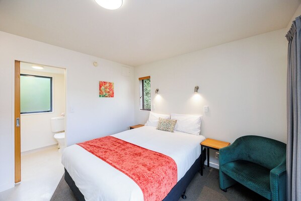 Una habitación de hotel con una cama, una silla, un ventanal y una puerta.