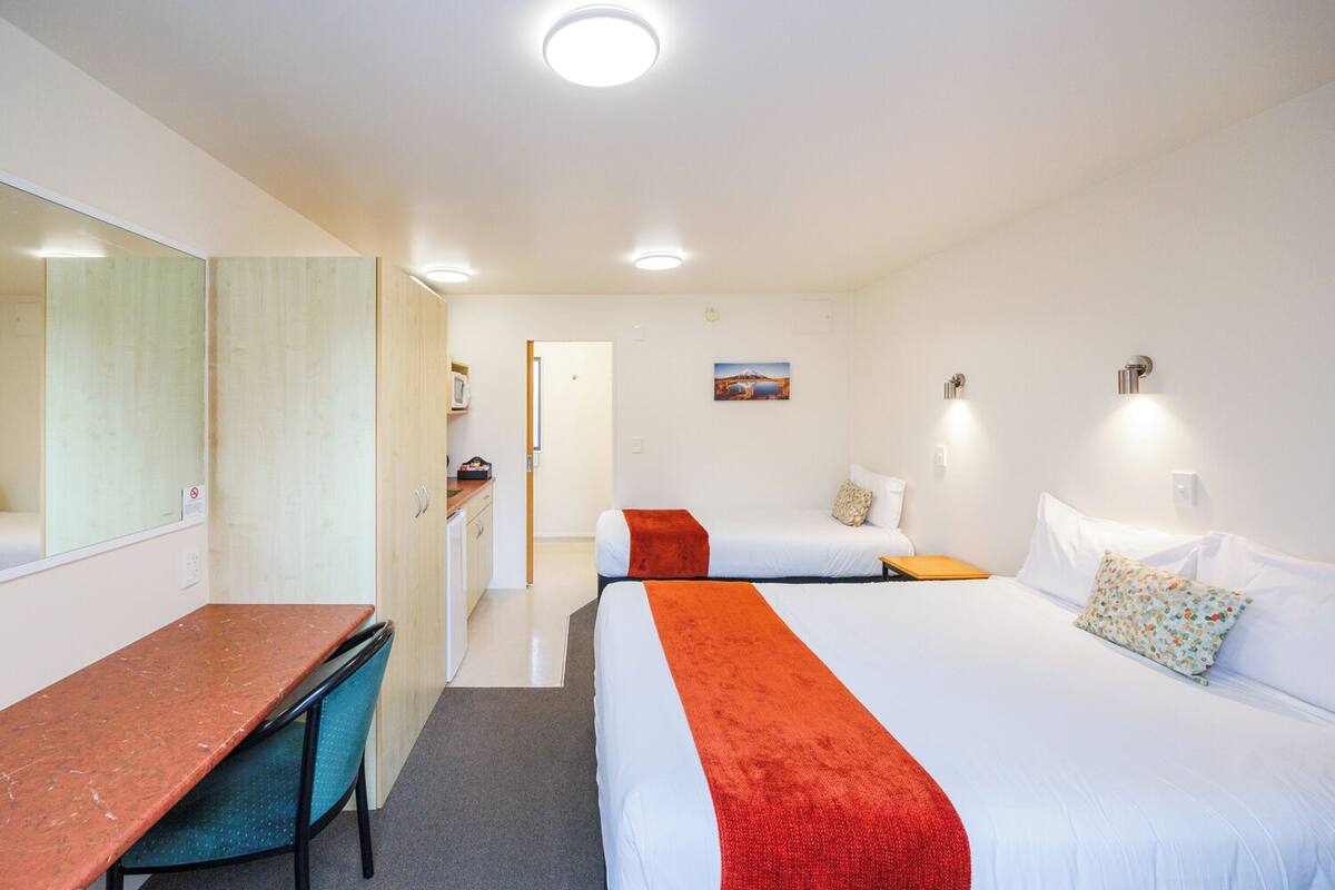 Quarto de hotel com escrivaninha, duas camas, uma kitchenette pequena e um banheiro.